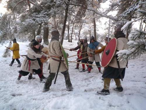 Photo: Vor der Kulisse eines verschneiten Kiefernwaldes trainieren Krieger und Kriegerinnen in Gewandung Linienkämpfe.