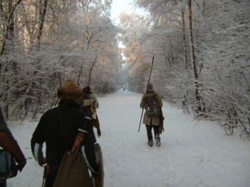 Photo: Die Kamera schaut einigen Kämpfern über die Schulter, wie sie mit gepackten Sachen auf einem baumgesäumten Weg in der Winterlandschaft ihre Heimreise antreten.